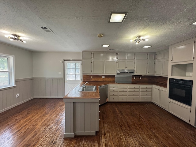 kitchen featuring dark wood finished floors, a sink, a wainscoted wall, black appliances, and under cabinet range hood