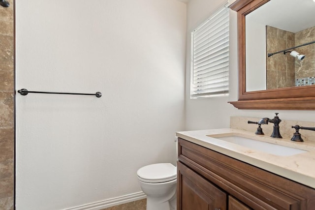 bathroom with baseboards, toilet, a tile shower, and vanity