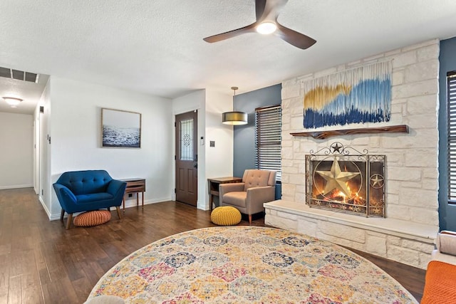 living area featuring a textured ceiling, baseboards, a fireplace, ceiling fan, and wood-type flooring