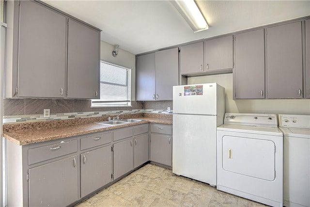 kitchen featuring gray cabinetry, washer and clothes dryer, a sink, and freestanding refrigerator