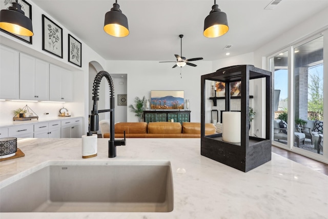kitchen featuring open floor plan, hanging light fixtures, a sink, white cabinets, and light stone countertops