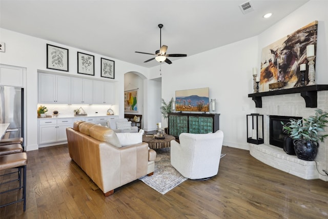 living room with dark wood finished floors, arched walkways, ceiling fan, visible vents, and a fireplace