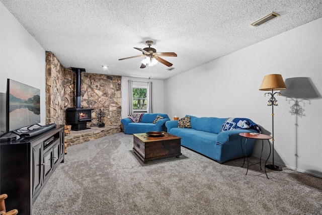 living room with a wood stove, a textured ceiling, a ceiling fan, visible vents, and carpet floors
