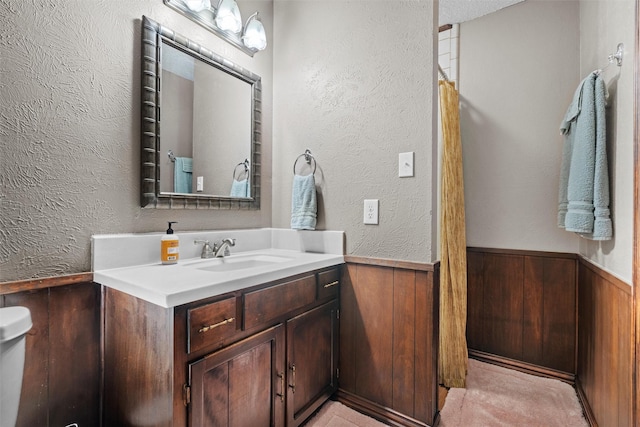 full bathroom featuring vanity, a textured wall, a shower with curtain, wood walls, and wainscoting