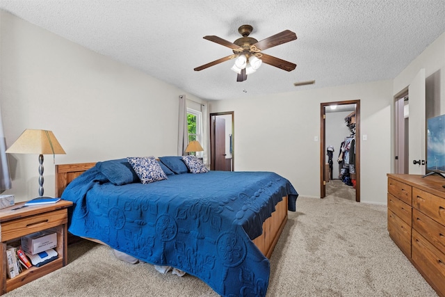 bedroom featuring ceiling fan, a textured ceiling, light colored carpet, a spacious closet, and visible vents