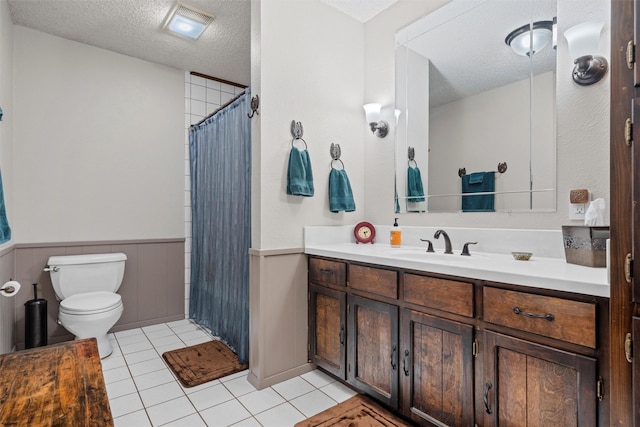 bathroom with a textured ceiling, vanity, a wainscoted wall, toilet, and tile patterned floors