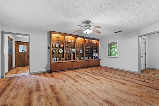 interior space with baseboards, a textured ceiling, visible vents, ceiling fan, and wood finished floors