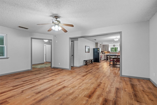 living area with ceiling fan, a textured ceiling, visible vents, light wood finished floors, and baseboards