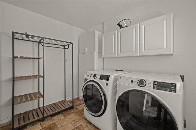 clothes washing area featuring washing machine and dryer, cabinet space, and stone finish flooring