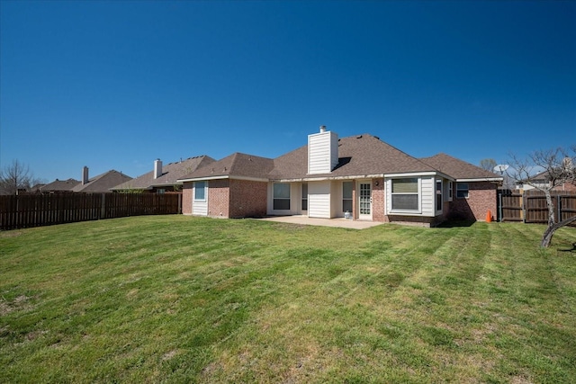 rear view of house with a fenced backyard, a patio area, brick siding, and a yard
