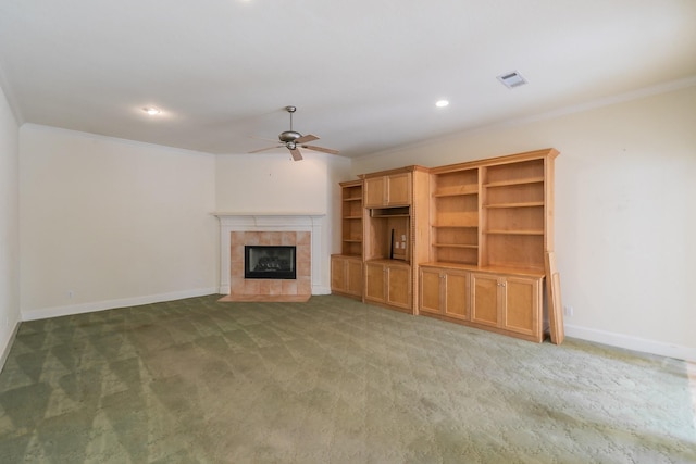 unfurnished living room with a tiled fireplace, ceiling fan, crown molding, baseboards, and light colored carpet