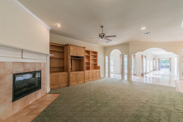 unfurnished living room with a tiled fireplace, decorative columns, visible vents, ornamental molding, and arched walkways