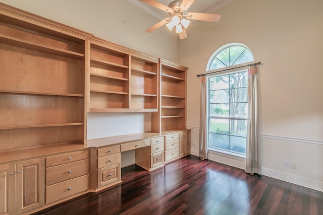 unfurnished office featuring lofted ceiling, built in study area, baseboards, a ceiling fan, and dark wood-type flooring