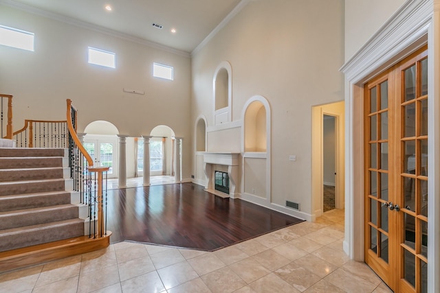 unfurnished living room featuring tile patterned flooring, a wealth of natural light, visible vents, crown molding, and a towering ceiling