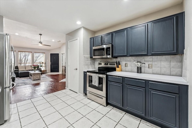kitchen with light countertops, ceiling fan, appliances with stainless steel finishes, open floor plan, and backsplash