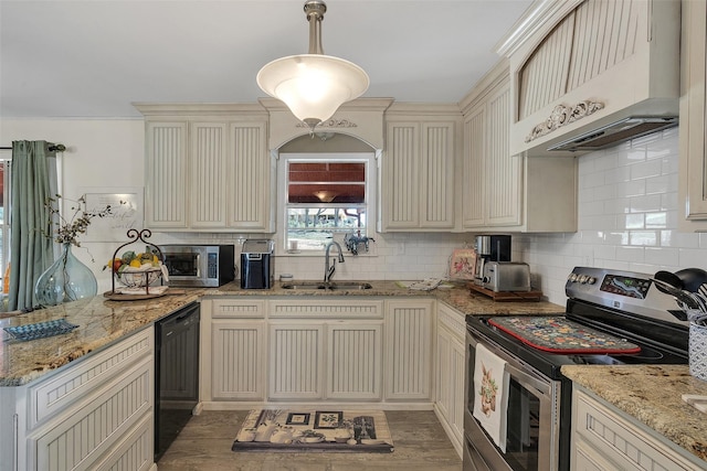 kitchen with cream cabinetry, a peninsula, stainless steel appliances, under cabinet range hood, and a sink