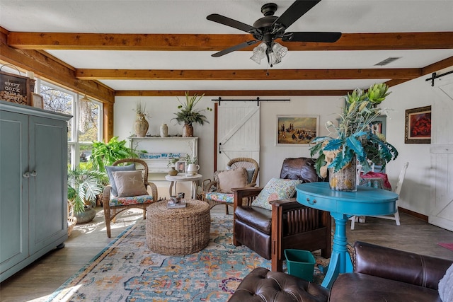 living area with wood finished floors, a barn door, beamed ceiling, and visible vents