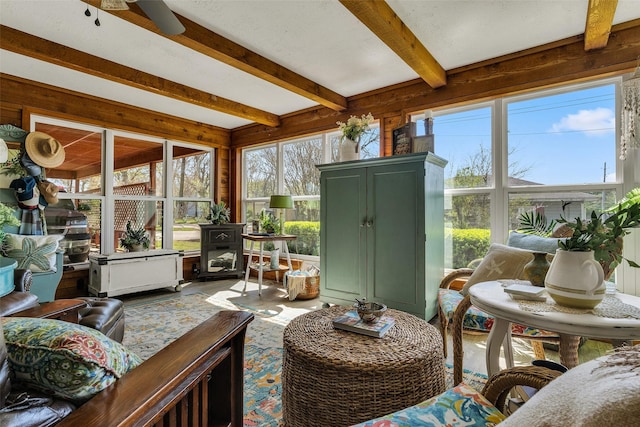 sunroom / solarium featuring plenty of natural light, beamed ceiling, and a wood stove