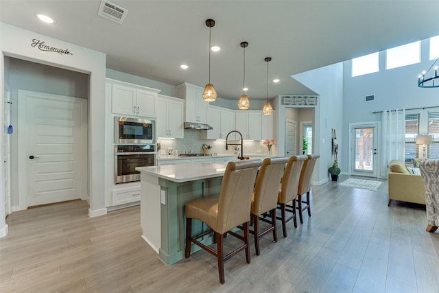 kitchen featuring tasteful backsplash, visible vents, light countertops, under cabinet range hood, and appliances with stainless steel finishes
