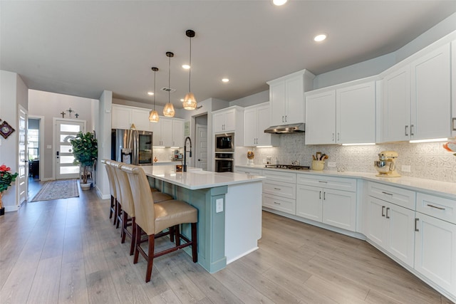 kitchen featuring tasteful backsplash, a breakfast bar, stainless steel appliances, light countertops, and under cabinet range hood