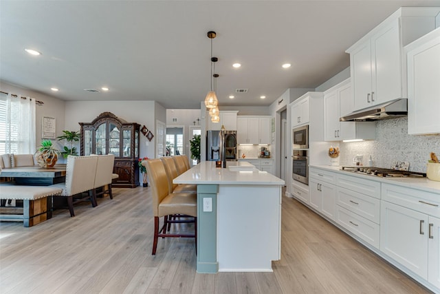 kitchen featuring stainless steel appliances, under cabinet range hood, a sink, and a wealth of natural light