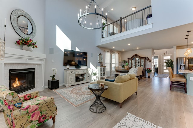 living area with a high ceiling, baseboards, a glass covered fireplace, light wood-style flooring, and a notable chandelier