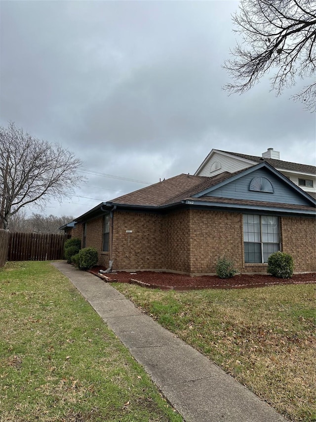 view of property exterior featuring brick siding, fence, and a lawn