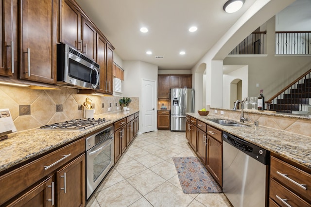 9721 Stripling Dr, Fort Worth, TX 76244 - kitchen with appliances with stainless steel finishes, a sink, light stone counters, arched walkways, and tasteful backsplash