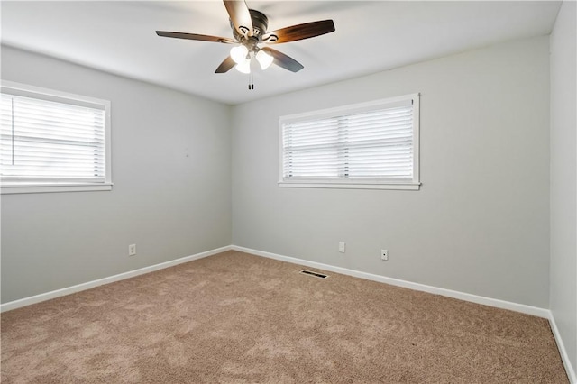 carpeted spare room with plenty of natural light, baseboards, visible vents, and ceiling fan