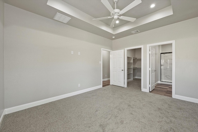 unfurnished bedroom featuring a tray ceiling, a spacious closet, baseboards, carpet floors, and a closet