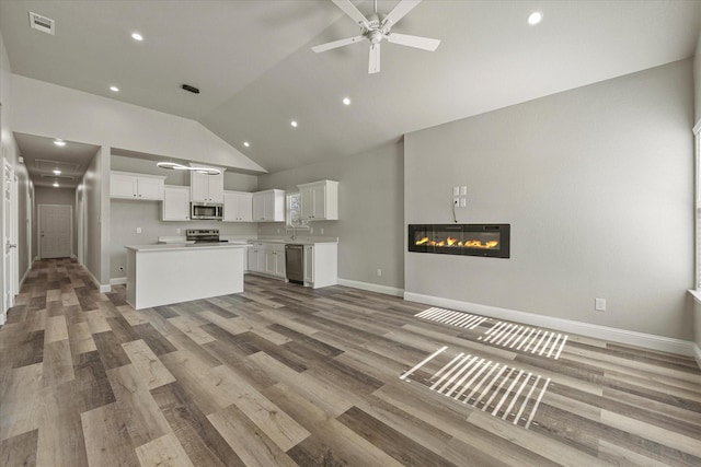 kitchen with open floor plan, white cabinetry, light wood-type flooring, stainless steel appliances, and a glass covered fireplace