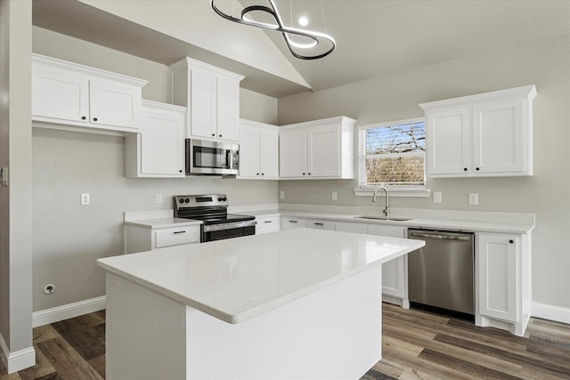 kitchen featuring stainless steel appliances, lofted ceiling, white cabinetry, a sink, and a center island