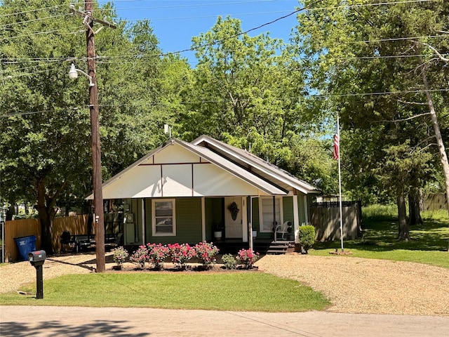 bungalow-style house featuring covered porch, fence, and a front lawn