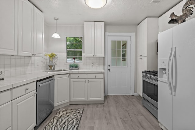 kitchen with light wood-style flooring, stainless steel appliances, tile counters, white cabinets, and a sink