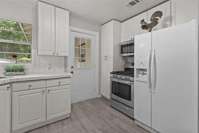 kitchen with visible vents, appliances with stainless steel finishes, white cabinets, light wood-type flooring, and tile countertops