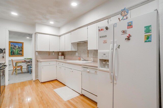 kitchen featuring white cabinets, light countertops, a sink, and white appliances