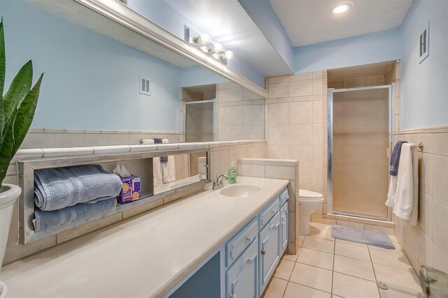 bathroom featuring tile patterned flooring, vanity, tile walls, toilet, and a stall shower