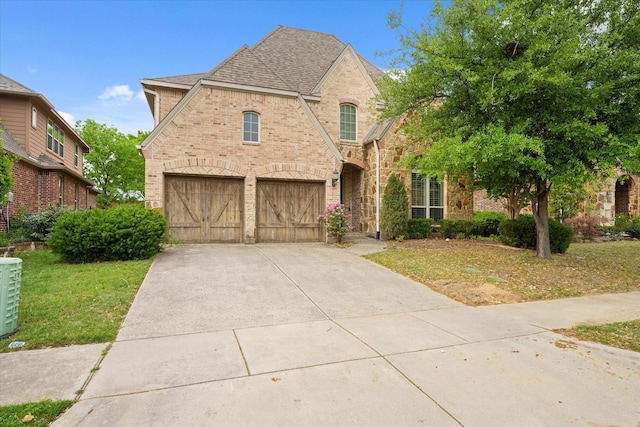 view of front facade featuring concrete driveway, a front lawn, a shingled roof, a garage, and brick siding
