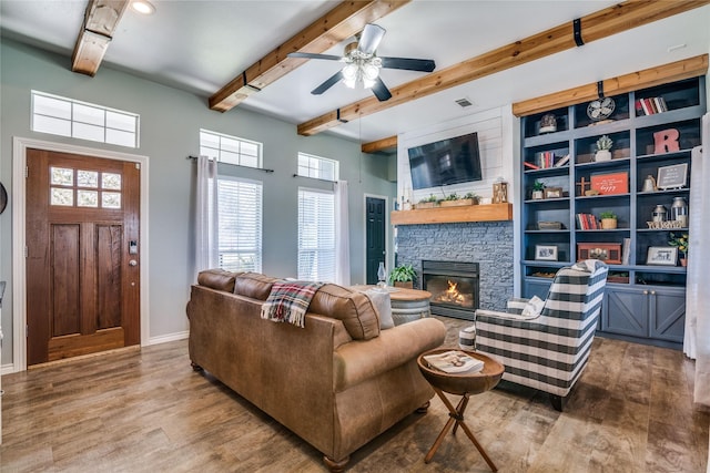 living area with baseboards, beam ceiling, a ceiling fan, a fireplace, and wood finished floors