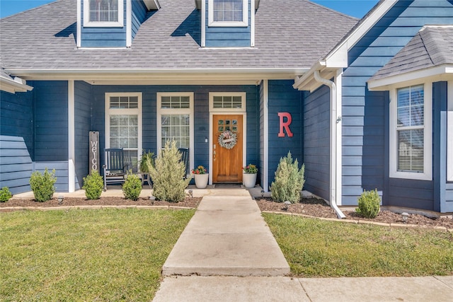 entrance to property with a yard, covered porch, and roof with shingles