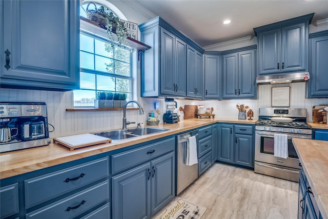 kitchen featuring a sink, butcher block countertops, blue cabinets, under cabinet range hood, and stainless steel appliances