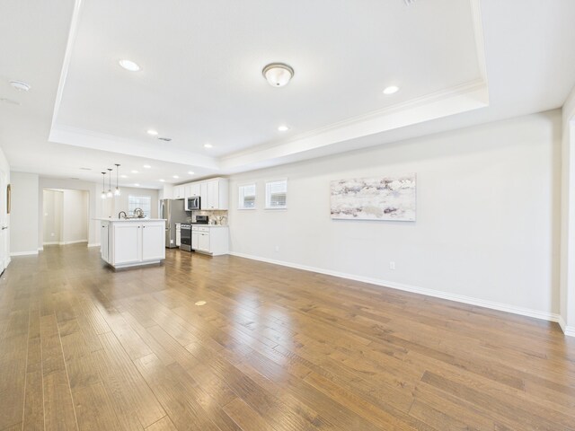 unfurnished living room featuring crown molding, a tray ceiling, baseboards, wood-type flooring, and recessed lighting