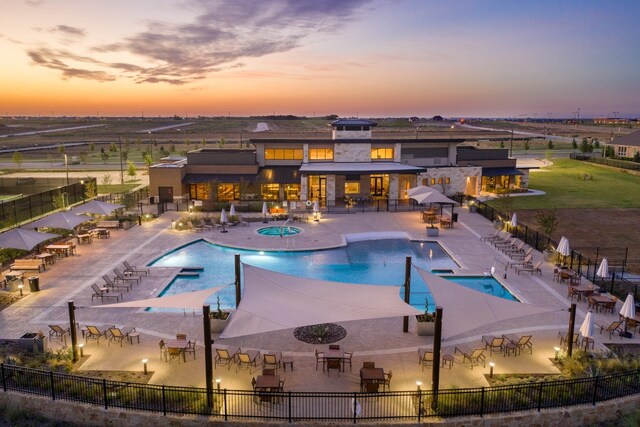 pool at dusk featuring a patio, fence, a community hot tub, and a community pool