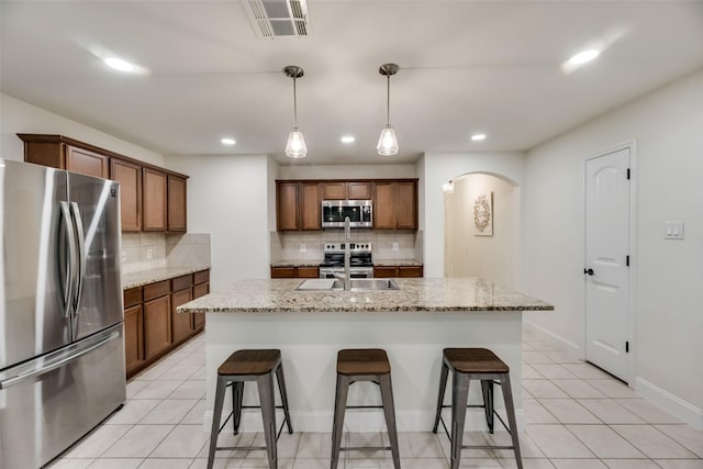 2282 Torch Lake Dr, Forney, TX 75126 - kitchen featuring arched walkways, a breakfast bar area, stainless steel appliances, and brown cabinetry