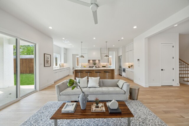 living room with light wood-type flooring, ceiling fan, stairs, and recessed lighting
