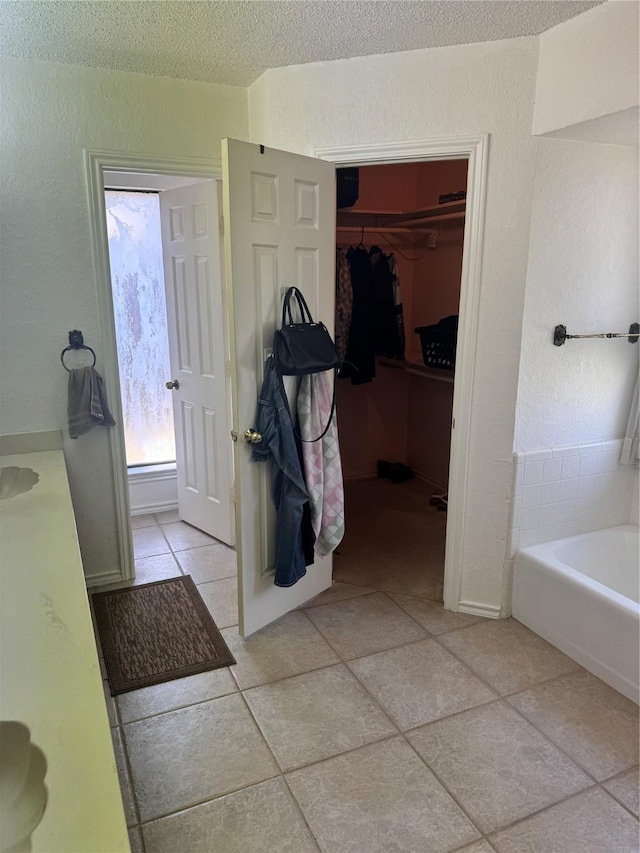 901 Freestone Ct, Arlington, TX 76017 - bathroom featuring a textured ceiling, tile patterned floors, a walk in closet, and a garden tub