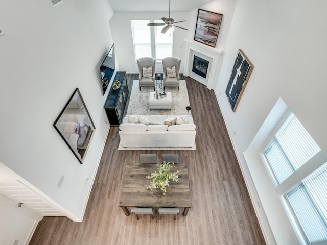 living area with a towering ceiling, wood finished floors, a fireplace, baseboards, and ceiling fan