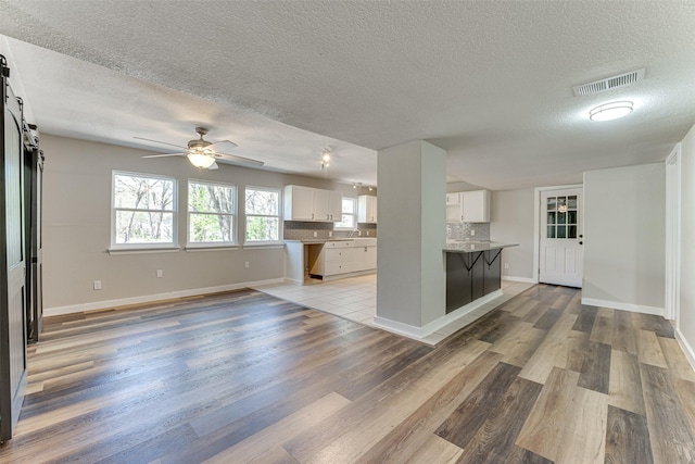 interior space featuring visible vents, white cabinets, a barn door, a breakfast bar, and backsplash