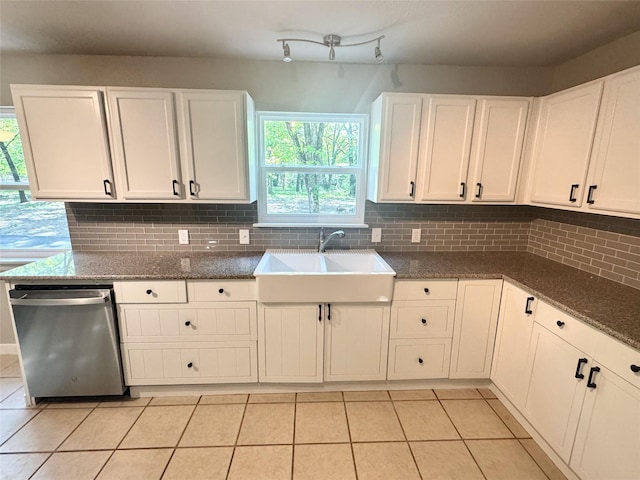 kitchen featuring stainless steel dishwasher, light tile patterned floors, white cabinetry, a sink, and backsplash