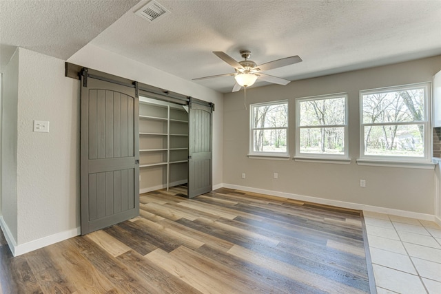 unfurnished bedroom featuring a textured ceiling, baseboards, visible vents, and a barn door
